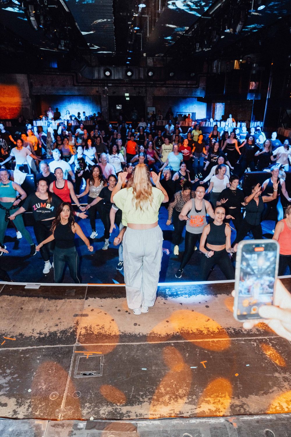 Blick von der Bühne: Lisa von hinten, vor ihr eine volle Halle tanzender Menschen
